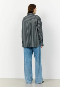 Striped button-up shirt in dark tones, featuring long sleeves and a relaxed fit, paired with high-waisted, wide-leg light blue jeans.