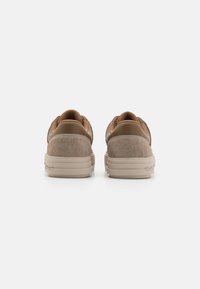 Tan suède en leren sneakers hebben een gladde textuur, ronde vorm en een minimalistisch ontwerp met een beige rubberen zool.