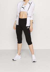 Vit lättvikts zipjacka, svarta korta joggers och vita sneakers. Logotypdetaljer på jackan och byxorna; figursydd atletisk design.