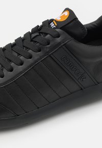 Must värvi nahast tenniseking tekstureeritud ülemise osaga, kontrastsete mustade triipudega ja musta kummist tallaga. Omab Camperi logo sildikest oranžis ja mustas.