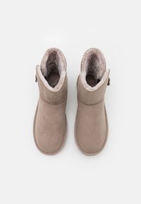Bottines beiges en daim doux, avec une doublure en peluche et des accents cousus autour de l'ouverture, dotées d'un détail de zip sur le côté.