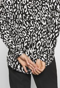 Sort og hvid leopardprint skjorte med lange ærmer og knapmanchetter, der har en afslappet pasform og glat stof, parret med sorte bukser.