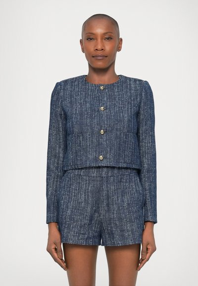 Ensemble deux pièces texturé bleu marine composé d'une veste courte avec des boutons dorés et d'un short ajusté, réalisé dans un tissu tissé avec un motif subtil.
