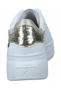 Valkoiset tennarit paksulla pohjalla ja metallinhohtoisella kultaisella halkeilevalla kantapäällä, nähtynä takaa.