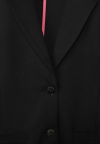 Černý blazer s klopovým límcem, s jedním knoflíkem, texturovanou tkaninou a kontrastní růžovou podšívkou.