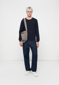 Navy long-sleeve shirt with a chest pocket, paired with wide-leg blue jeans and white sneakers. Gray crossbody bag slung over shoulder.
