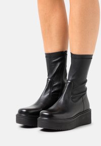 Bottes courtes en cuir noir avec une finition douce et texturée. Elles présentent une fermeture éclair latérale, un bout arrondi et une semelle épaisse en caoutchouc plat.
