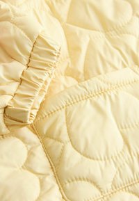 Tissu matelassé jaune arborant des motifs en forme de cœur, avec un bord froncé offrant une texture et une finition douce.