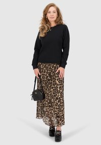 Felpa nera, gonna plissettata con stampa leopardata, scarpe nere con plateau, piccola borsa nera con dettagli dorati. Texture lisce e motivi audaci.