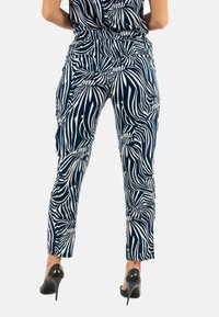 Pantaloni blu navy con un motivo a foglie bianche, design a gamba affusolata, vita elastica e due tasche laterali, abbinati a tacchi alti neri.