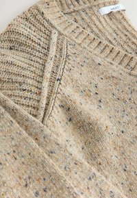 Beige strikket sweater med et tekstureret mønster, der har stænk af blå og orange. Ribbet halsudskæring og kantdetaljer er synlige.