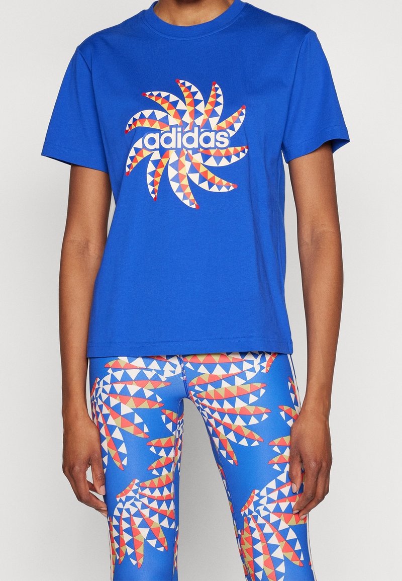 Blå bomull t-shirt med ett vitt och flerfärgat geometriskt mönster och logotyp framtill; tillsammans med blå leggings med mönster som har liknande designer.