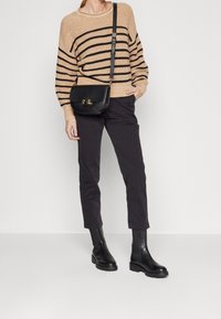 Suéter de rayas beige, bolso cruzado negro, pantalones ajustados negros y botines negros con suela gruesa. Tejido texturizado y diseño estructurado.