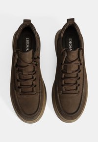 Baskets marron avec une tige en cuir texturé, bout rond et lacets plats. Semelle en caoutchouc épaisse avec un motif subtil sur le bord. Logo à l'intérieur.
