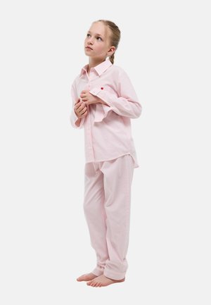 Jeune fille debout pieds nus en pyjama rose clair à rayures, regardant vers le haut et tenant le col de sa chemise des deux mains.