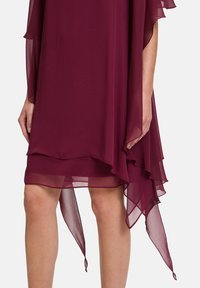 Burgunderfarbendes Chiffonkleid mit transparenten, schichtweisen Ärmeln und asymmetrischem Saum. Die glatte Textur und das fließende Design schaffen eine elegante Silhouette.