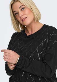 Black sweater with a textured, sequined diamond pattern. Features a crew neckline and ribbed cuffs. Worn with a gold bracelet.