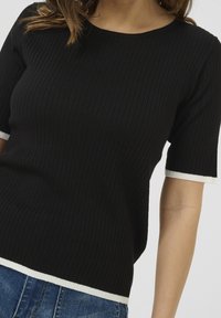 Top de punto negro con relieve y manga corta, con un escote redondeado y un acabado en contraste blanco en las mangas y el dobladillo.