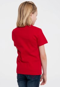 Red short-sleeved t-shirt made of cotton, featuring a classic crew neck and a smooth texture. Worn with navy denim jeans.