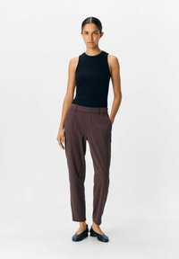 Svart ribbet tank topp og kastanjefargede skreddersydde bukser. Antrekket har en tettsittende design og glatt tekstur, sammen med svarte leiligheter.