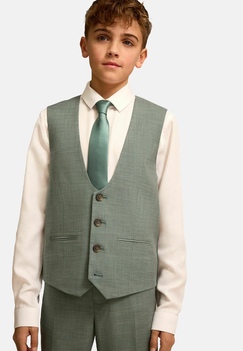 Garçon portant un gilet de costume vert clair et une cravate assortie sur une chemise blanche, regardant droit devant avec une expression neutre.