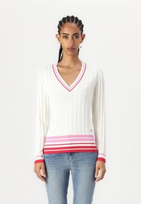 Maglione bianco a coste con scollatura a V, con dettagli a strisce rosse, rosa e bianche lungo l'orlo e i polsini delle maniche. Tessuto a maglia morbido.