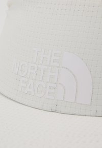White bucket hat made of textured material, featuring a prominent embossed logo "THE NORTH FACE" in glossy white on the front panel.