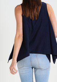 Top senza maniche blu navy realizzato in tessuto leggero, con una vestibilità ampia e orlo asimmetrico, abbinato a jeans skinny blu chiaro.