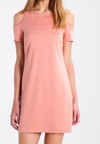 Sukienka z krótkim rękawem i odkrytymi ramionami w miękkim brzoskwiniowym materiale. Gładka tekstura, luźny krój, okrągły dekolt i długość do połowy uda.