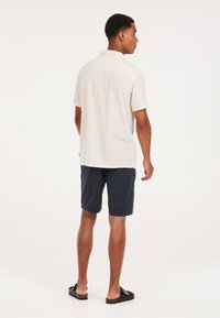 Lichtgekleurde, gestreepte short-sleeve shirt met een kraag, gecombineerd met marineblauwe shorts en zwarte sandalen. Het shirt heeft een relaxed fit en een textuurstof.