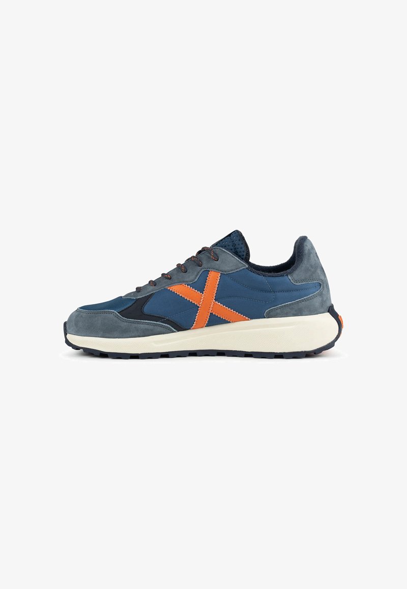 Baskets bleu marine et gris avec détail orange "X", semelle blanche rembourrée, bande de roulement noire et design à lacets.