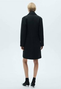 Sort frakke med en skræddersyet design, der har en bred krave og strukturerede skuldre. Stoffet ser glat ud og har en længde til midten af låret.