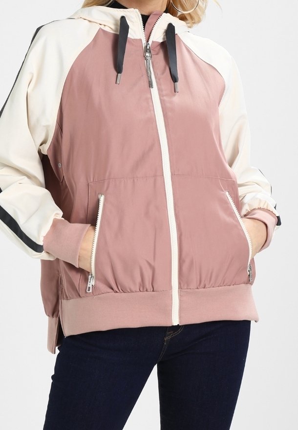 Kevyt, kaksivärinen takki vaaleanpunaisena ja kermanvärisenä, jossa on vetoketjukiinnitys, huppu ja sivutaskut. Pehmeä rakenne, jossa on kontrastivärisiä mustia yksityiskohtia.