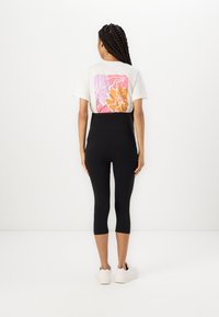 Sorte leggings med høy midje kombinert med en hvit t-skjorte som har et flerfarget abstrakt design på baksiden.