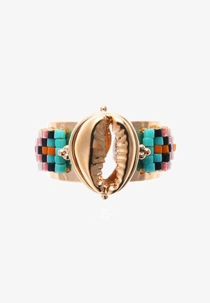 Golden cuff bracelet featuring a cowrie shell centerpiece, with colorful beaded accents in turquoise, coral, and black, arranged in a woven pattern.