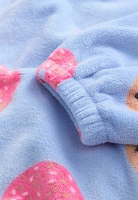 Blå fleece tæppe med pink og røde jordbærmønstre. Blød tekstur med samlede manchetter og en glat, fyldig finish.