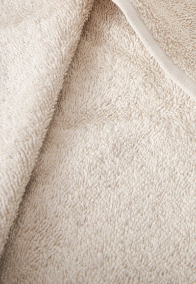 Gros plan sur un tissu éponge doux de couleur crème avec des boucles visibles et un bord plié.