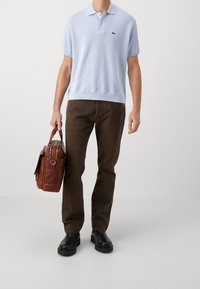 Ljusblå stickad polotröja, mörkbruna byxor, svarta skor, håller en brun läderväska med dubbla handtag, med dragkedja och metallaccenter.