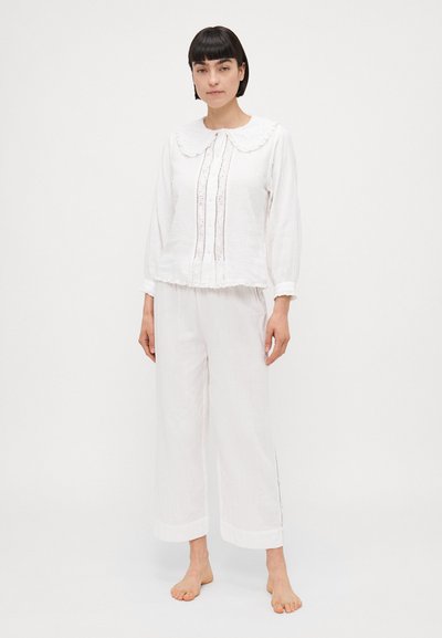 Hvidt bomulds-loungewear sæt med krave-top og dekorative syninger samt bredbenede bukser med sideskæringer. Blødt, struktureret stof.