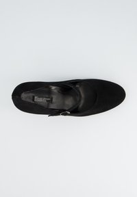 Chaussure en daim noir avec un bout arrondi, une bride sur le pied et une petite boucle. Doublure en cuir lisse avec une semelle plate.