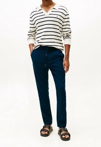 Pruhované polo s dlouhým rukávem v krémové a námořnické barvě s výstřihem do V. Tmavě modré, volné kalhoty s elastickým pasem, doplněné černými sandály.