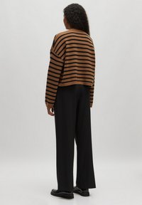 Bruin en zwart gestreept cropped sweater met losse mouwen, gecombineerd met zwarte wijde broek en zwarte schoenen. Gladde gebreide stof.