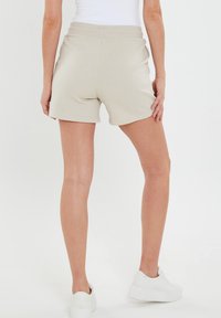 Pantaloni corti beige in cotone con vita elasticizzata, tasche laterali e un design semplice. Abbinati a sneaker bianche.