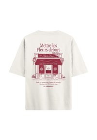 Lichtbeige t-shirt met een rode grafische print van een bloemenwinkel, inclusief tekst en potplanten aan beide zijden van de ingang.