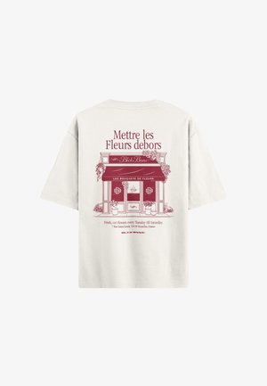 Hellbeige T-Shirt mit rotem grafischem Design, das einen Blumenladen darstellt, einschließlich Text und Topfpflanzen auf beiden Seiten des Eingangs.