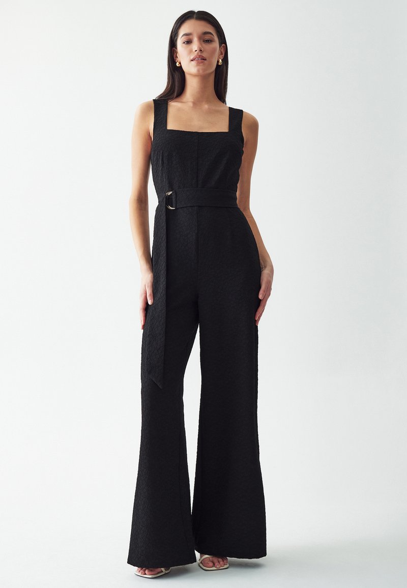 Mono negro con un acabado texturizado, escote cuadrado, diseño de pierna ancha y un cinturón de tela con hebilla redonda.