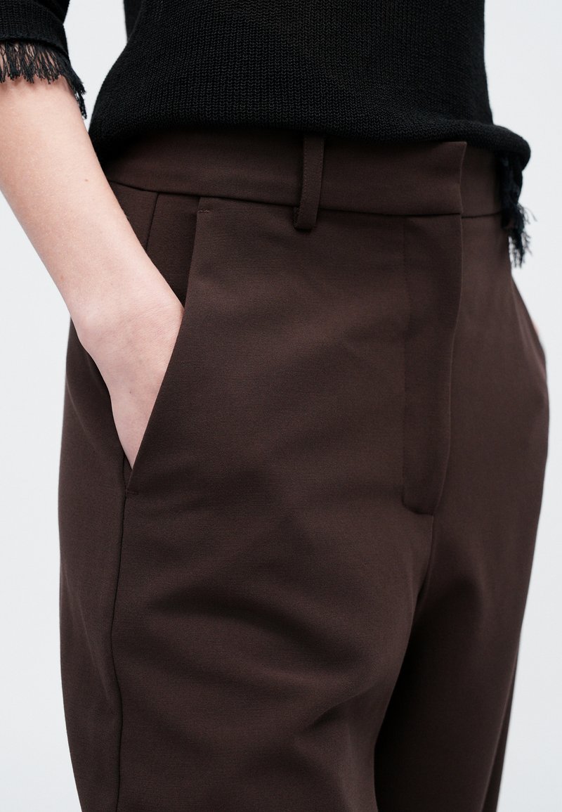 Pantaloni marroni su misura con tasche laterali, tessuto liscio e vita aderente. Presentano un design semplice e pieghe sottili.