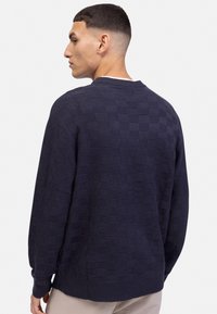 Granatowy sweter o teksturze z wzorem w szachownicę, luźny krój, okrągły dekolt i ściągacze. Tkanina z mieszanki bawełnianej, minimalistyczny design.