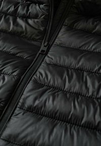 Svart puffer väst med kviltad design, med en slät, glänsande yta och dragkedja fram. Ingen synlig branding eller detaljer.