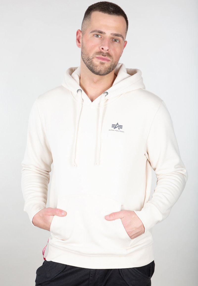 Sudadera blanca con capucha, bolsillos frontales, cordón ajustable y un pequeño logotipo gris en el pecho. Tejido suave y diseño ajustado.